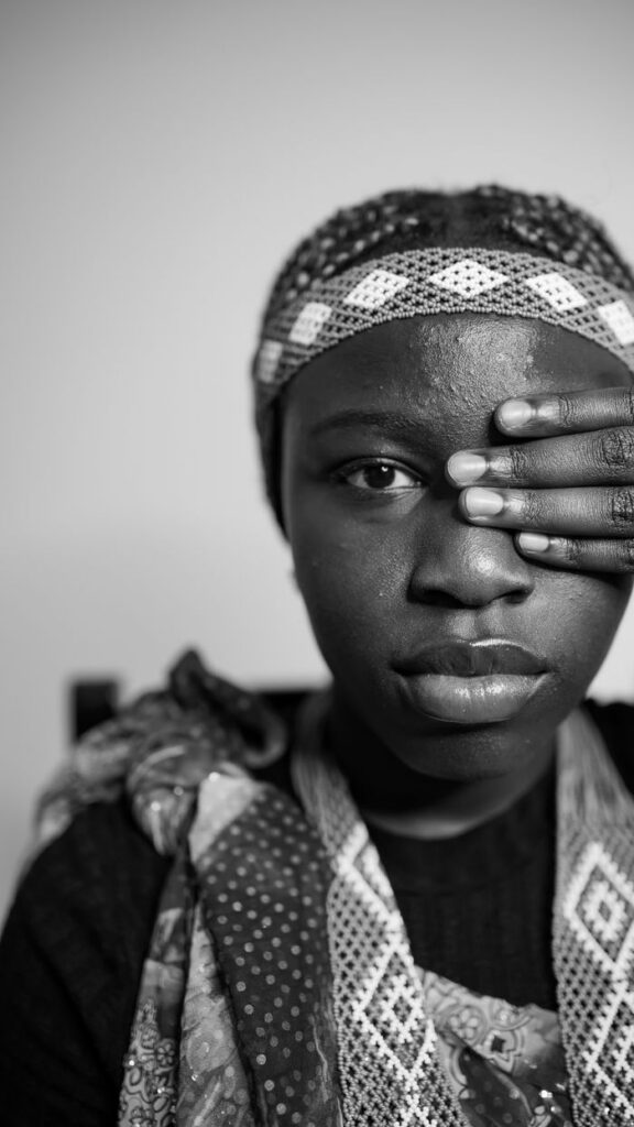 Monochrome portrait of a woman covering one eye with her hand.